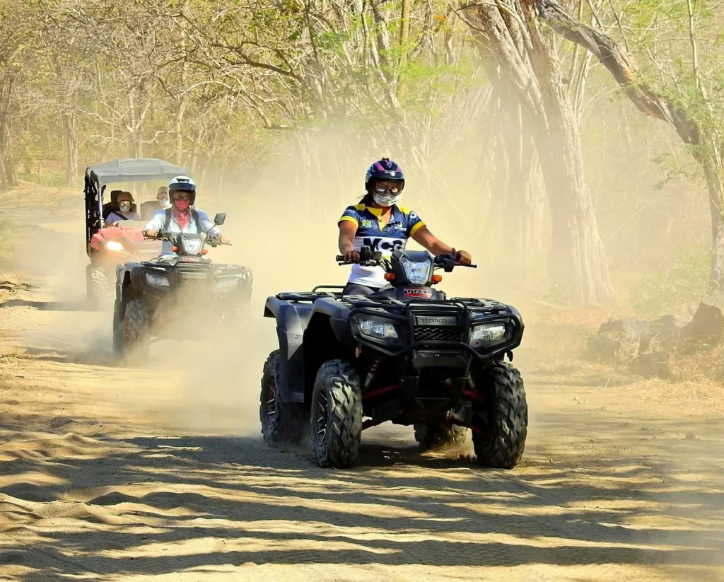 Riders on a full-size ATV and a buggy raising dust through the dry forest in the dry season at Congo Trail, Guanacaste