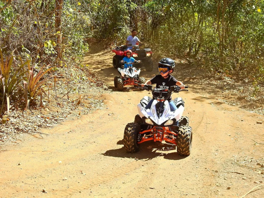 Children riding kid-sized ATVs on a dry-season forest trail with a guide at Congo Trail, Sardinal, Guanacaste, Costa Rica