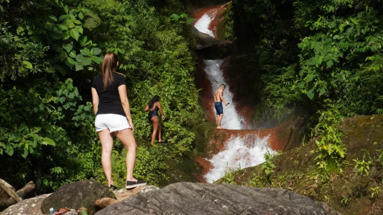 Hikers climbing beside a red-rock cascade on a waterfall tour near Miravalles