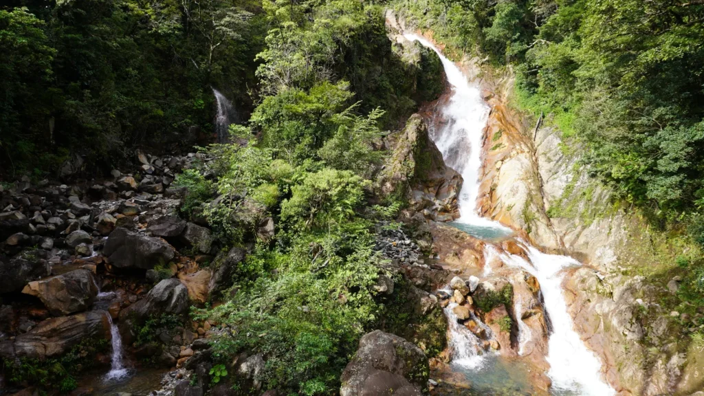 Mineral-rich volcanic waterfall cascading over orange rock on a Miravalles waterfall tour