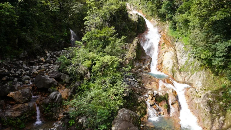 Mineral-rich volcanic waterfall cascading over orange rock on a Miravalles waterfall tour