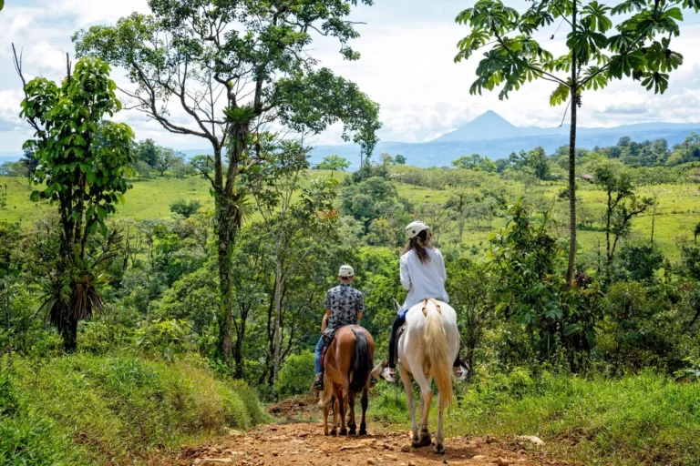 Riders taking in the rainforest valley with Arenal Volcano on the horizon, on a horseback tour above Río Celeste, Costa Rica