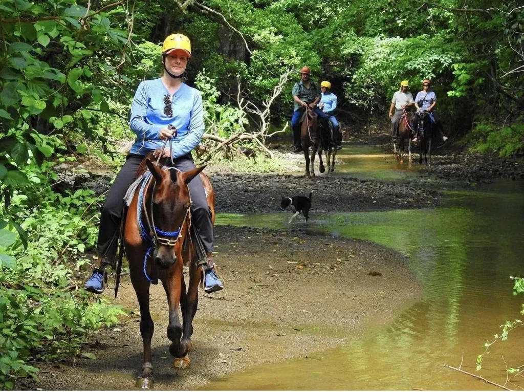 Riders and a local guide crossing a shallow stream on a horseback ride at Congo Trail, Guanacaste