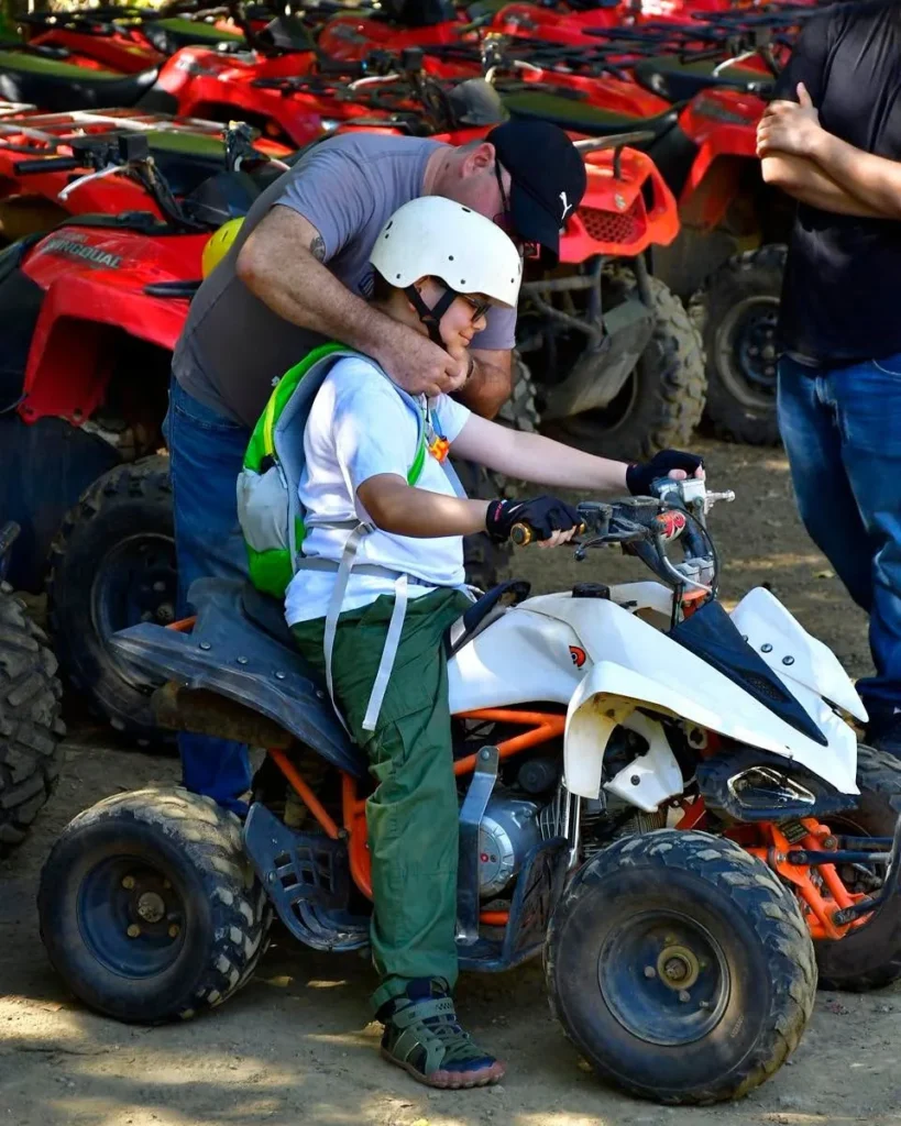 A local guide helping a child with a helmet on a kid-sized ATV at Congo Trail, Guanacaste, Costa Rica