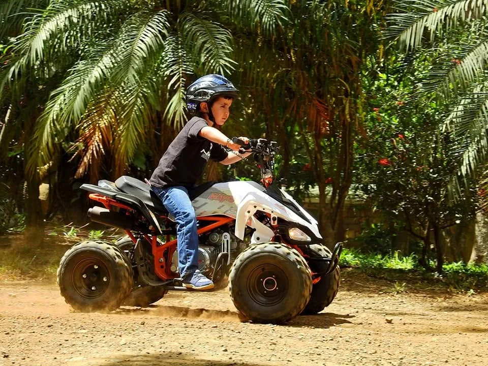 A child driving a kid-sized ATV past palms at Congo Trail, Sardinal, Guanacaste