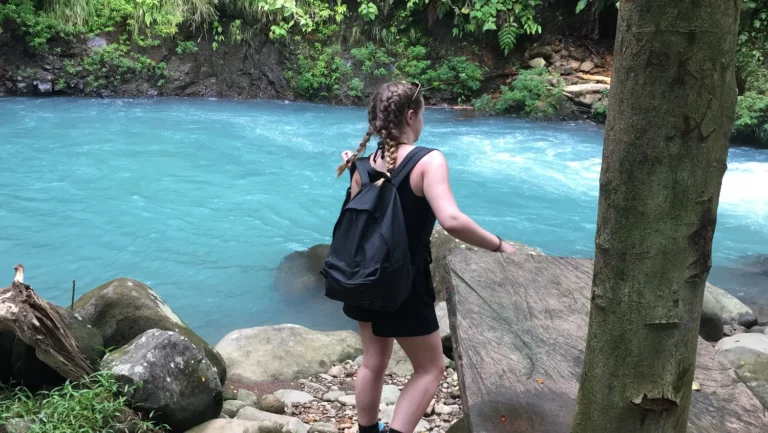 Hiker with a backpack on the rocks beside the turquoise Río Celeste at the swimming spot, Costa Rica