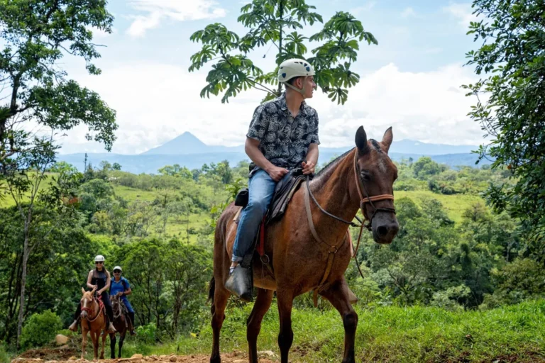 Rider on horseback with Arenal Volcano on the horizon, on the forested slopes above Río Celeste, Costa Rica