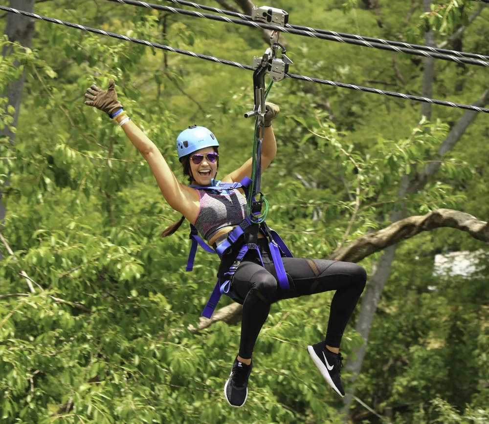 Smiling woman flying along a zip line through the forest canopy on a ziplining tour in Guanacaste, Costa Rica