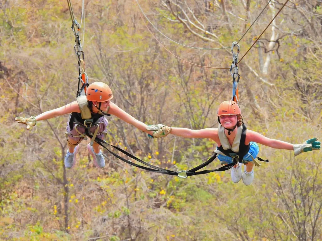 Two women zip lining together with arms outstretched on a canopy tour in Guanacaste, Costa Rica