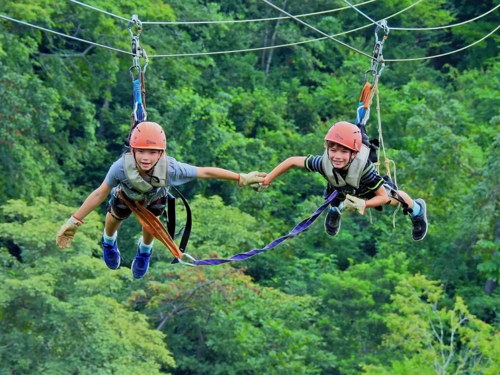 Two children zip lining side by side holding hands on a canopy tour in Guanacaste, Costa Rica