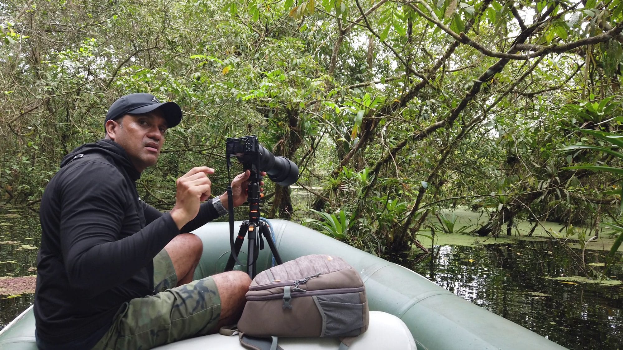 Miller Contreras adjusting a camera with telephoto lens while wildlife-watching from a boat on a rainforest lagoon in Costa Rica